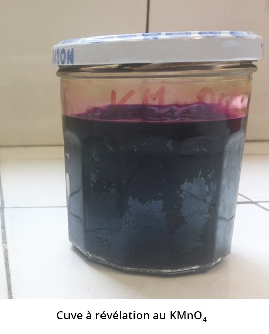 Photo d'un pot à confiture contenant un liquide violet. Le pot porte la mention manuscrite : KMnO4. La photo est sous-titrée : cuve à révélation au KMnO4.