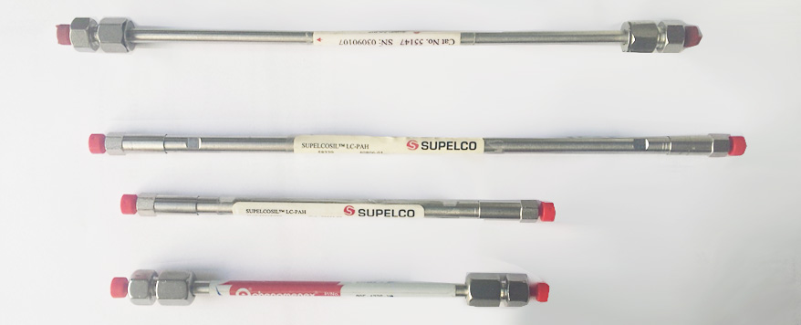 Picture showing 4 HPLC columns. They are metal tubes of different sizes, with nuts on the ends and red plastic caps. Each column has a label.