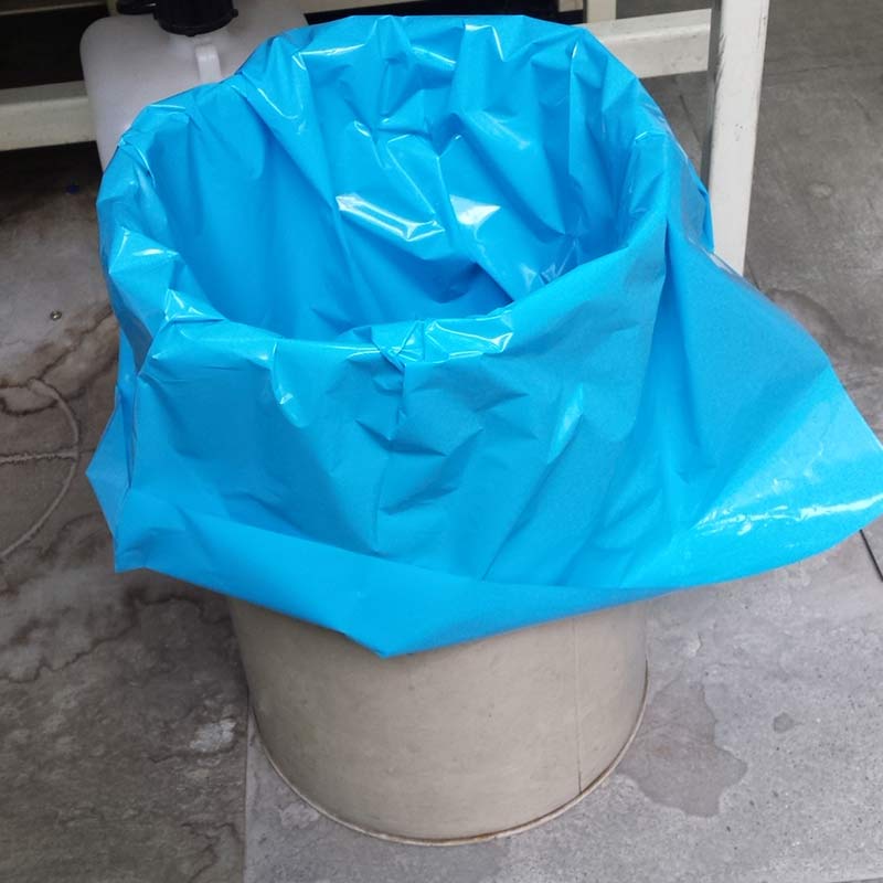 Picture of a garbage can on the ground containing a blue plastic bag